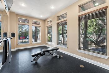 A gym room with a bench, weights, and windows. at Bridge at Heritage Woods, Austin, Texas